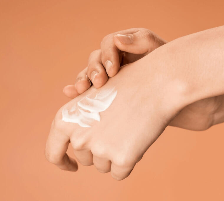 Applying nourishing hand cream on smooth skin against a warm, neutral background.